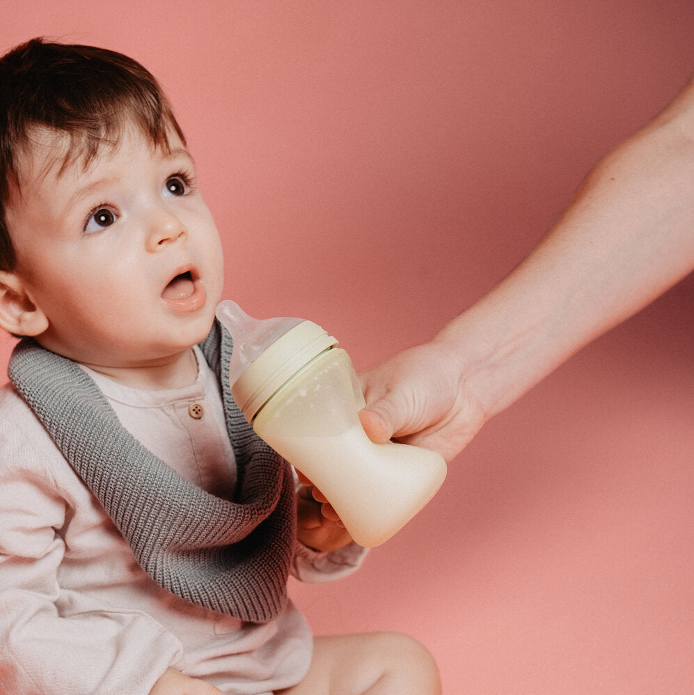 Baby holding a yellow Suavinex color essence bottle against a pink background
